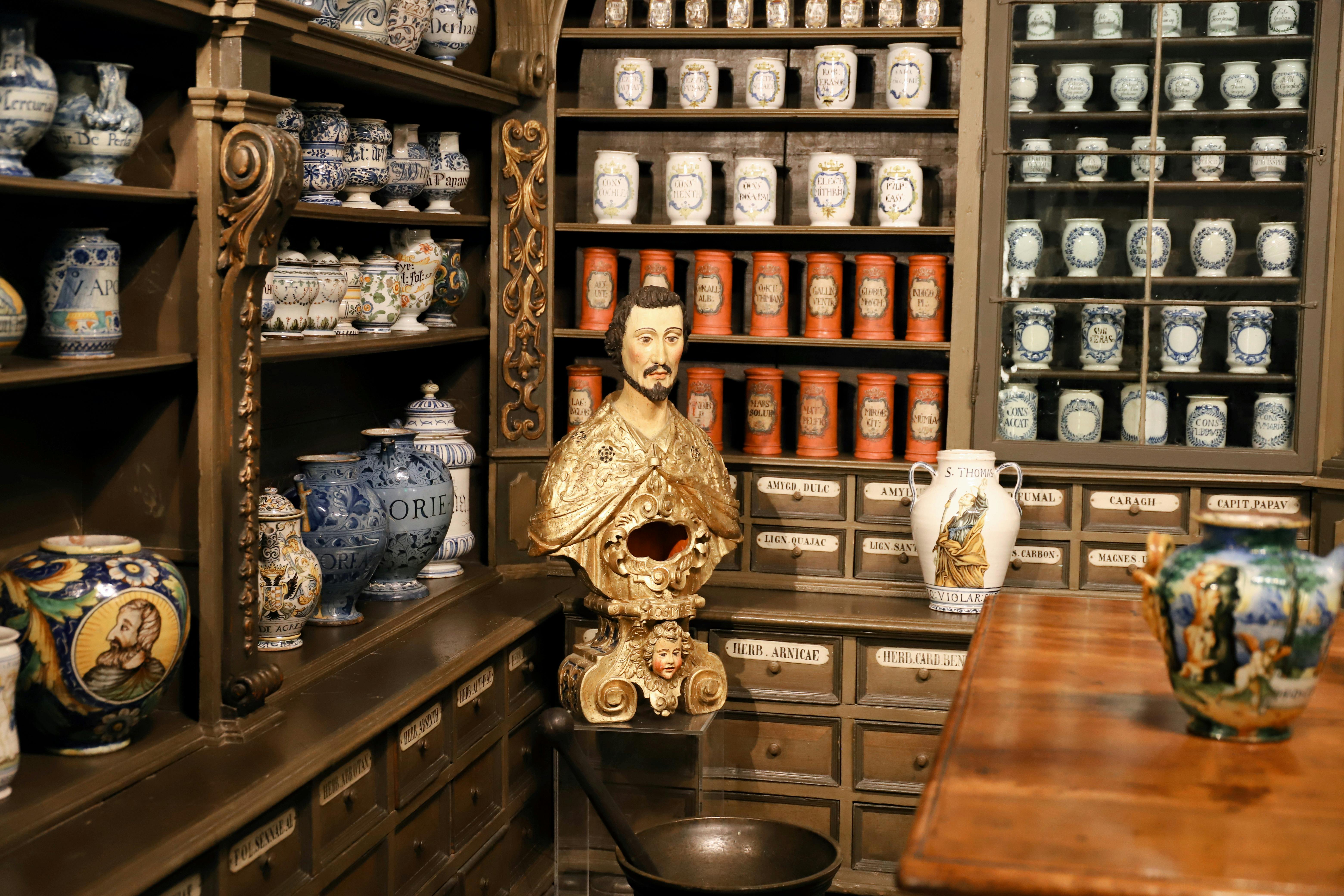 18th-century apothecary display at the German Pharmacy Museum in Heidelberg, with rows of labeled ceramic jars and a gilded bust